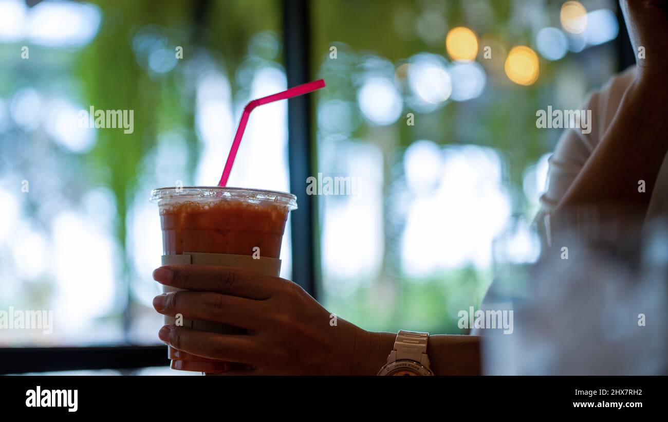 Les femmes tiennent main le thé glacé dans un verre en plastique au café. Boisson au thé glacé utilisant de la paille en plastique dans le café Lifetyle Banque D'Images