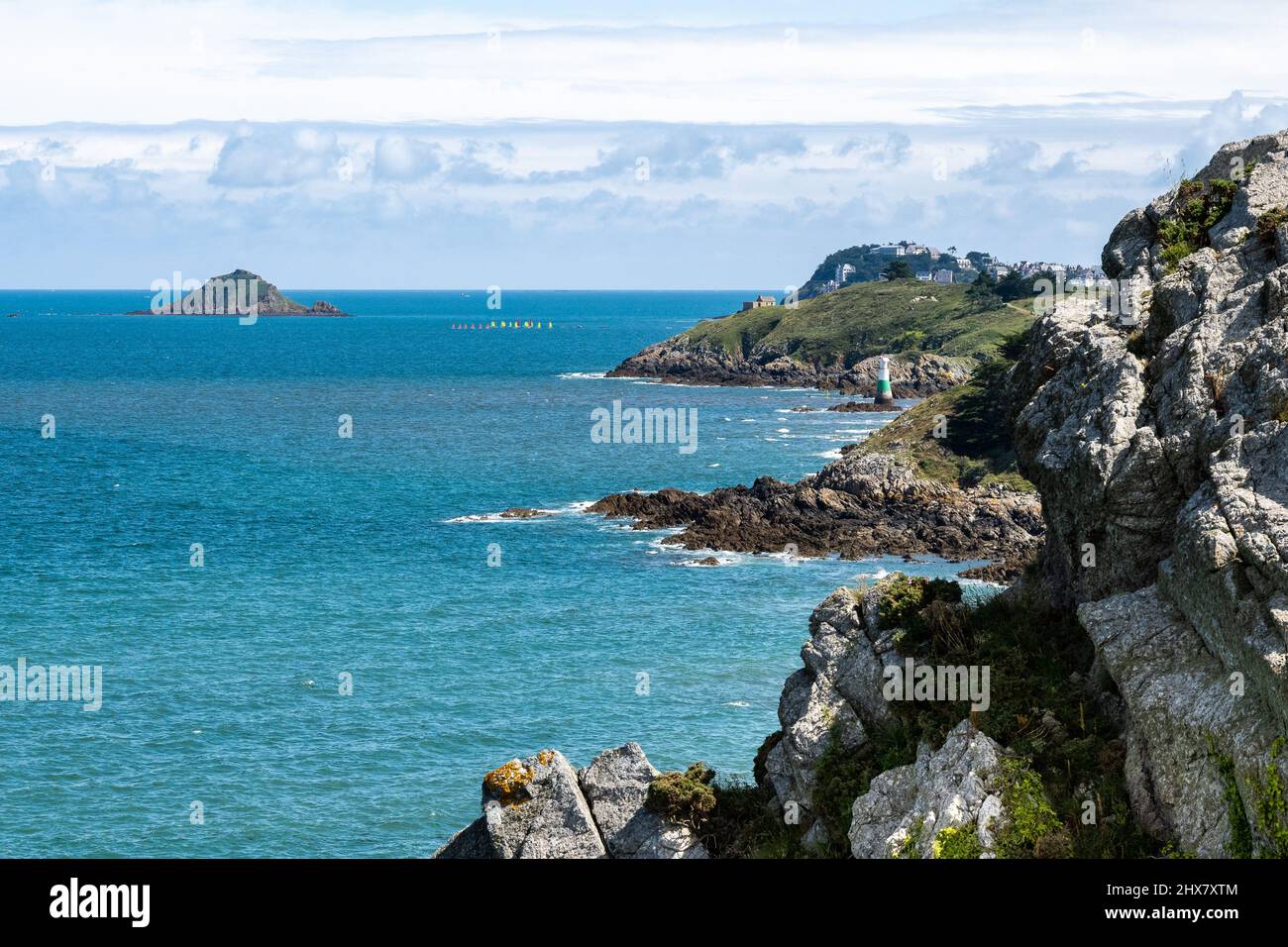 Des falaises gardées de verdure tombent précipitamment dans l'Atlantique bleu fort brillant dans le nord de la Bretagne.de petits voiliers flottent au soleil sur la mer. Banque D'Images
