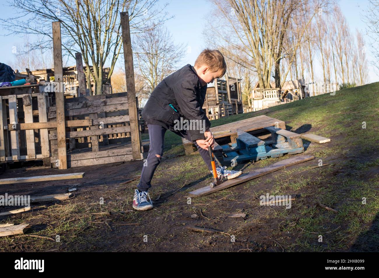 Un jeune garçon tente de retirer un clou d'une planche tout en construisant une cabane à partir de vieilles palettes, à fort Plankensteijn dans le terrain de jeux de Jeugdland à Amsterdam, aux pays-Bas. Banque D'Images