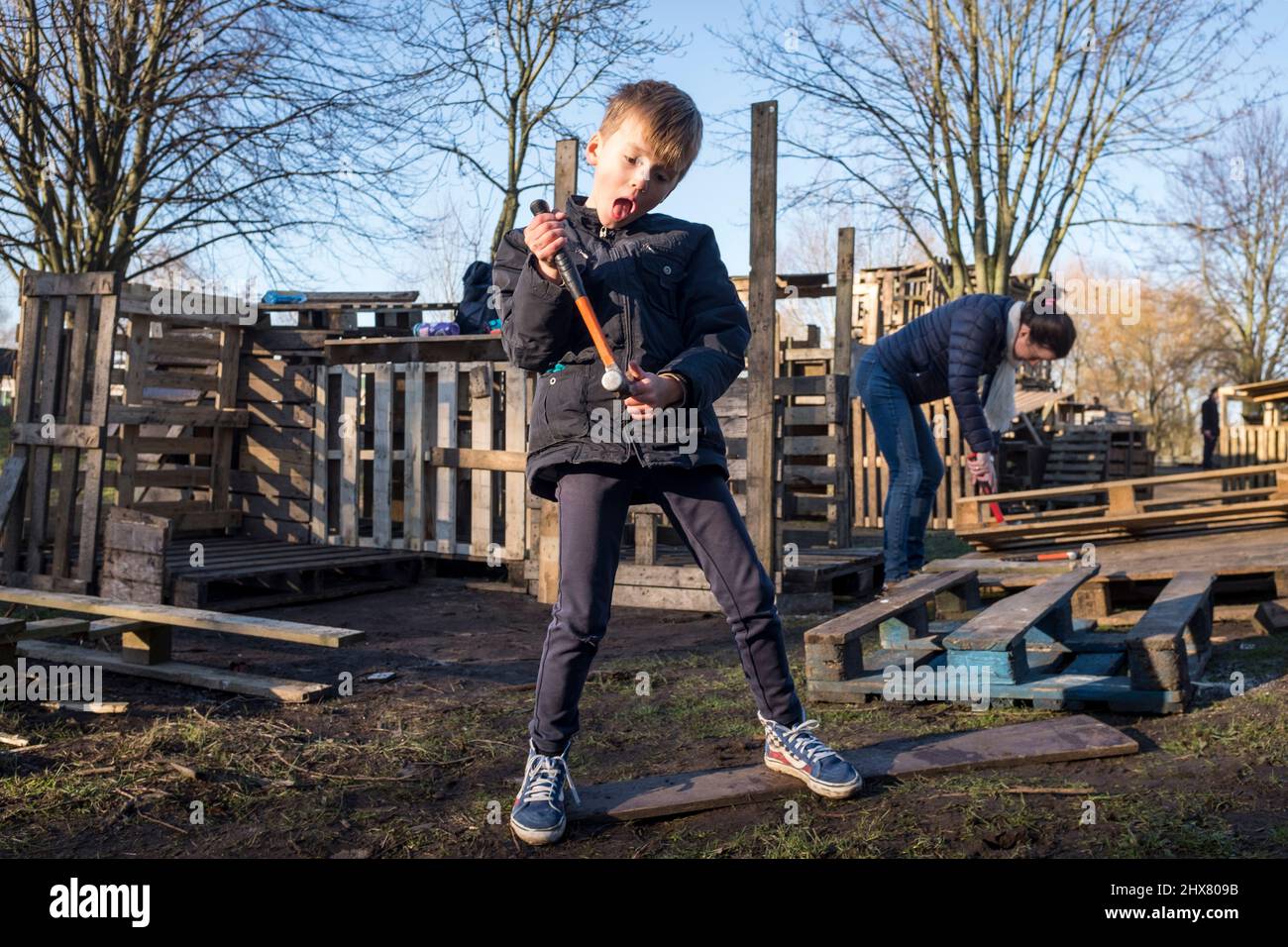 Un jeune garçon joue avec un marteau tout en construisant avec sa mère une cabane à partir de vieilles palettes, au fort Plankensteijn dans le terrain de jeux de Jeugdland à Amsterdam, aux pays-Bas. Banque D'Images