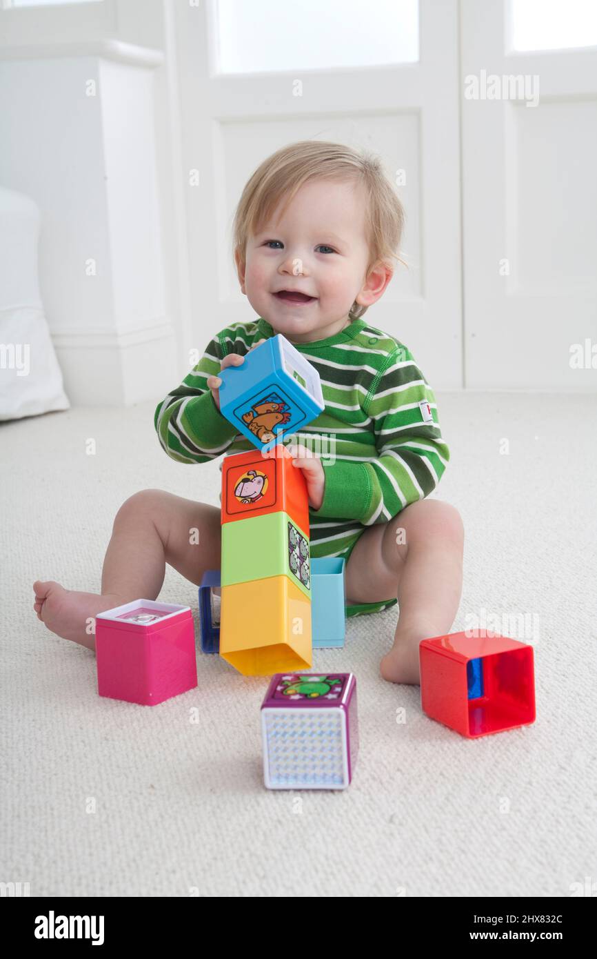 Bébé garçon assis sur la moquette jouant avec des blocs colorés Banque D'Images