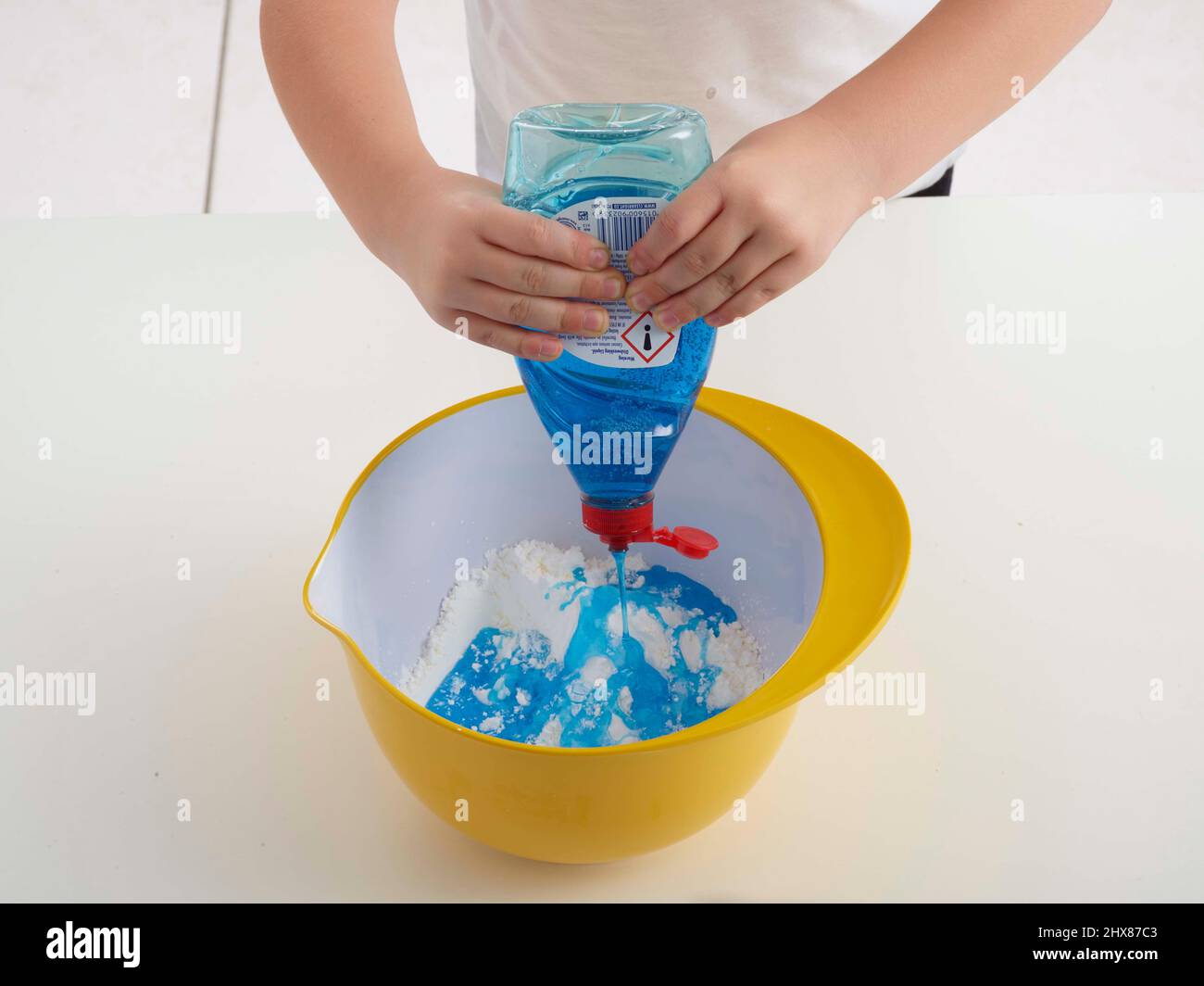 enfant versant du liquide de dévatation dans un bol de farine Banque D'Images