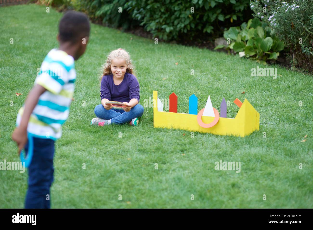 Les enfants jouent dans le jardin avec un jeu de jeu d'anneau en carton Banque D'Images