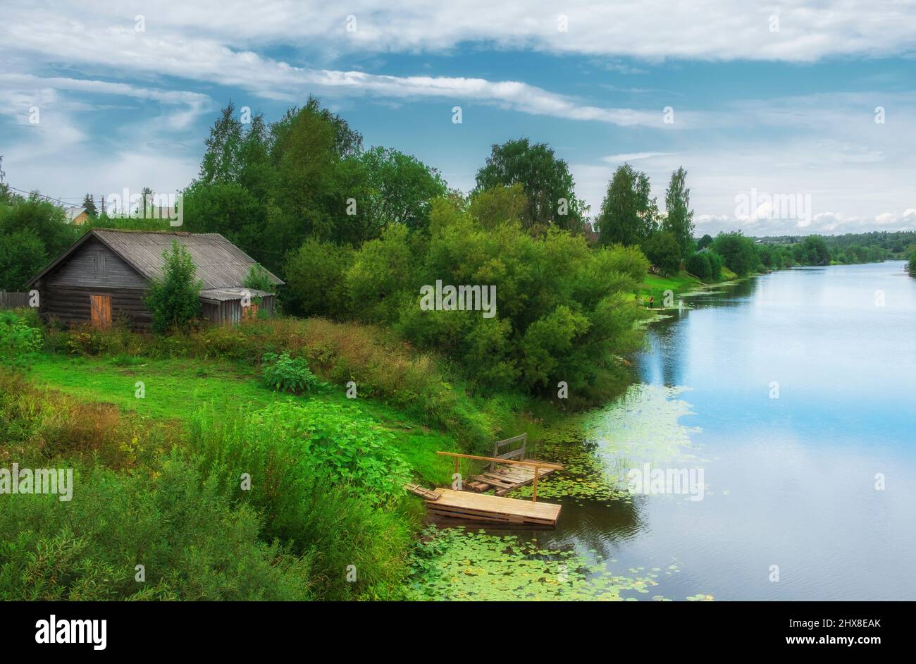 ancienne grange en bois sur la rivière avec une jetée. Été dans le village. Ciel bleu avec nuages et lumière du jour. Banque D'Images