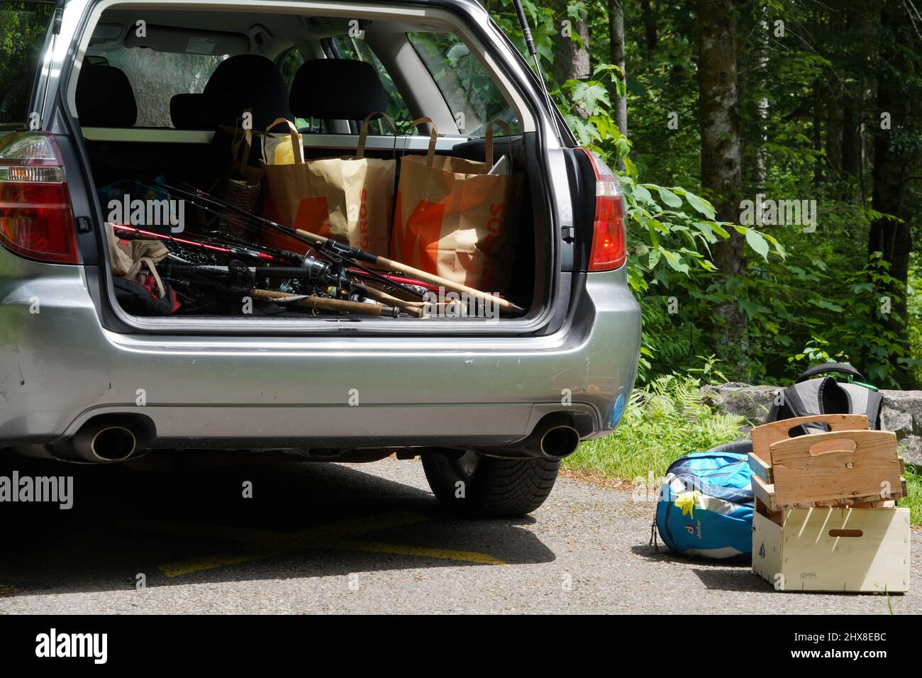 Espace de bagages d'une voiture pleine d'équipement de pêche. Il y a quelques sacs à dos et des étuis en bois à l'extérieur de la voiture placés sur le sol. Banque D'Images
