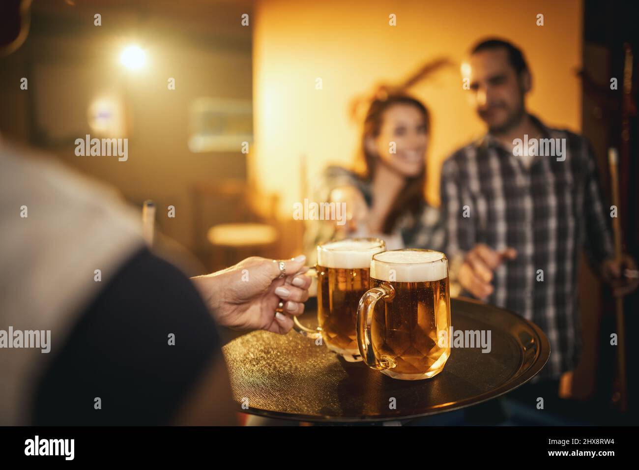 La serveuse sert de la bière à un couple souriant et joyeux joue au billard au bar après le travail. Banque D'Images
