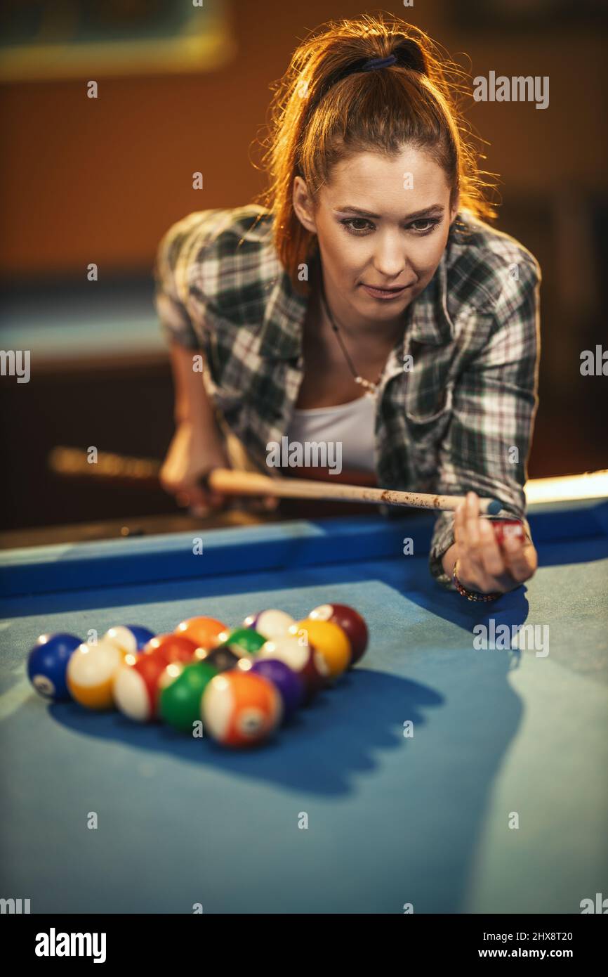 Jeune femme concentrée en jouant au billard dans le club de billard après le travail. Banque D'Images