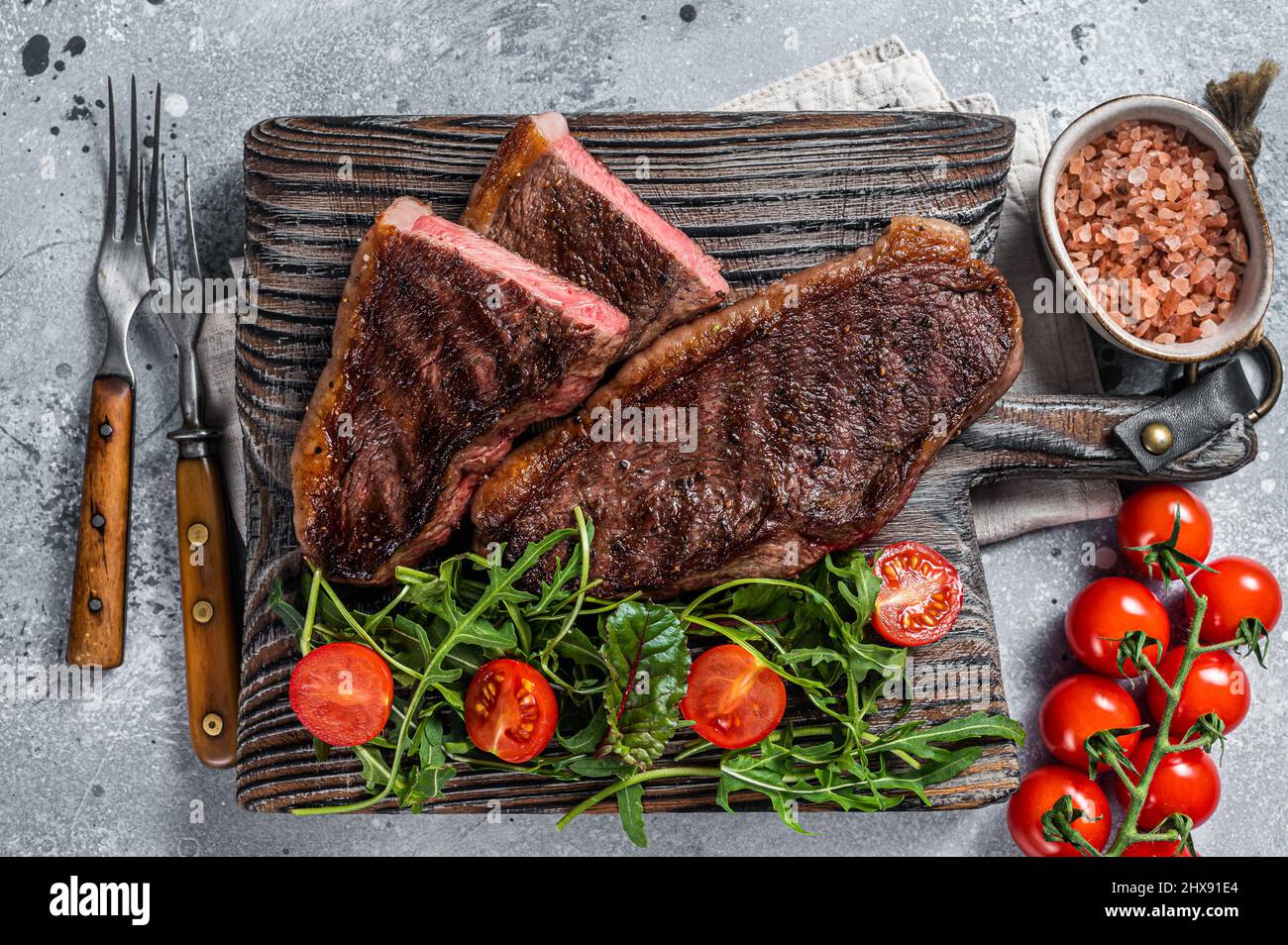 Steak de viande de bœuf rôti au chapeau ou au sirloin supérieur sur une planche de bois avec salade.Arrière-plan gris.Vue de dessus Banque D'Images