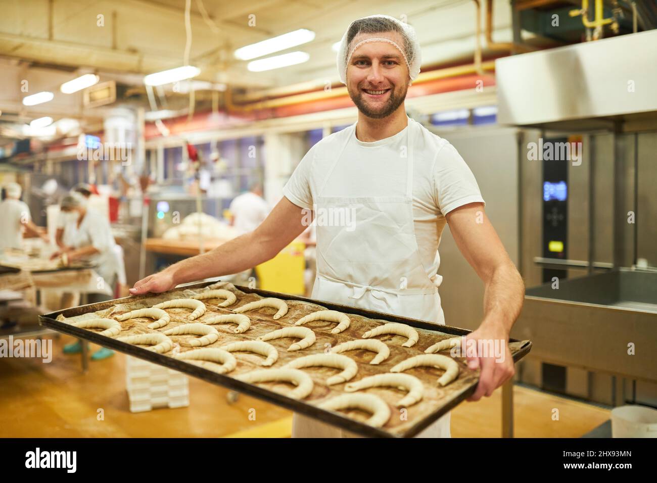 Jeune homme apprenti boulanger portant plaque de cuisson avec croissants dans la boulangerie Banque D'Images