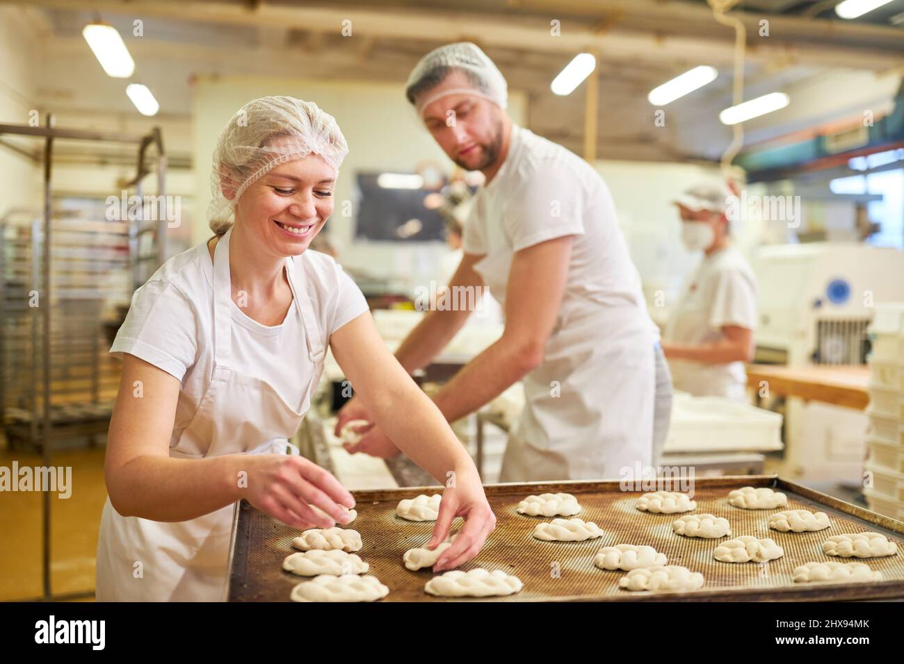 Les jeunes apprentis boulangers en équipe qui cuisent des plaques de levure sur une plaque de cuisson dans la boulangerie Banque D'Images