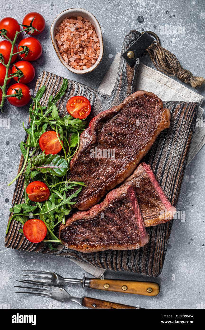 Steak de viande de bœuf rôti au chapeau ou au sirloin supérieur sur une planche de bois avec salade.Arrière-plan gris.Vue de dessus Banque D'Images
