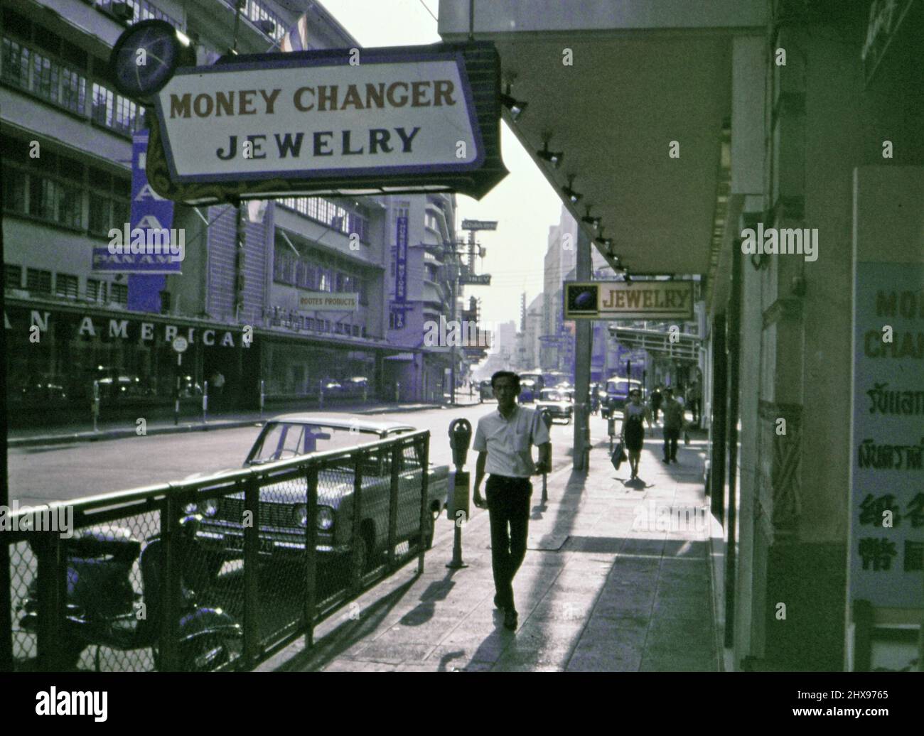 Scène de rue, homme marchant sur le trottoir devant un lieu de change, dans une ville asiatique non identifiée (éventuellement le Japon ou le Vietnam) à la fin de 60s ou au début de 1970s) Banque D'Images