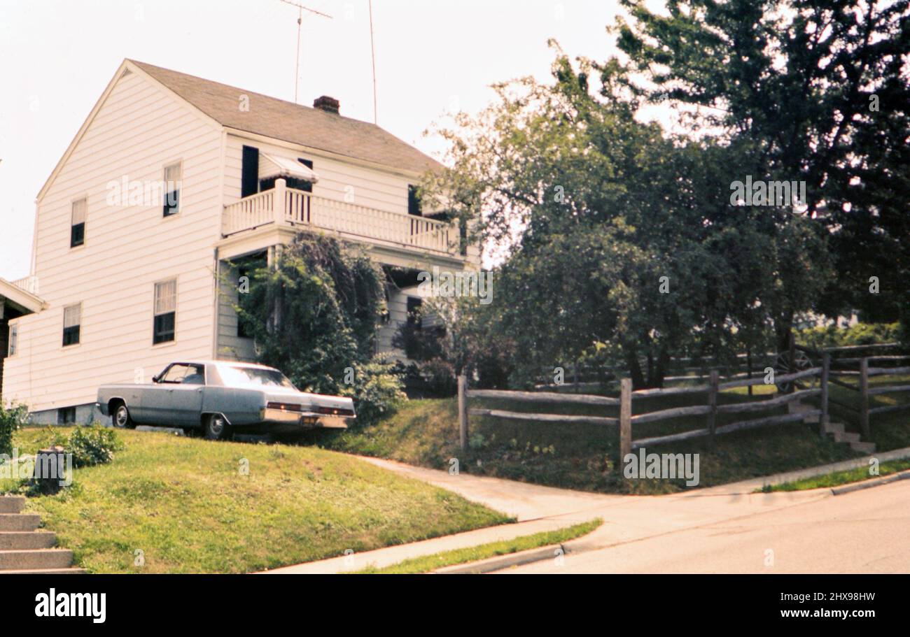 Voiture dans une allée à côté d'une maison avec ses feux de recul allumés car il quitte l'allée vers la fin de 60s ou début 1970s Banque D'Images