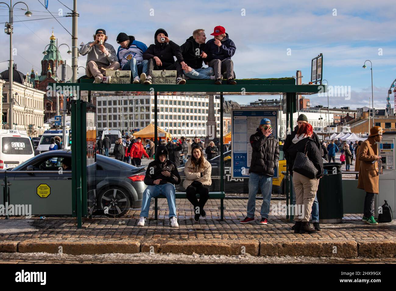 Les jeunes célèbrent la médaille d'or du hockey olympique en s'asseyant sur le toit d'un arrêt de tramway et en buvant de la bière à Helsinki, en Finlande Banque D'Images