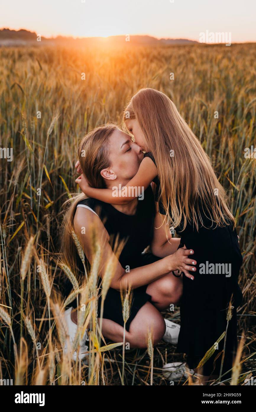 Enfant mignon embrassant sa mère sur un champ de blé doré au coucher du soleil d'été. L'été. Bonne famille au coucher du soleil Banque D'Images