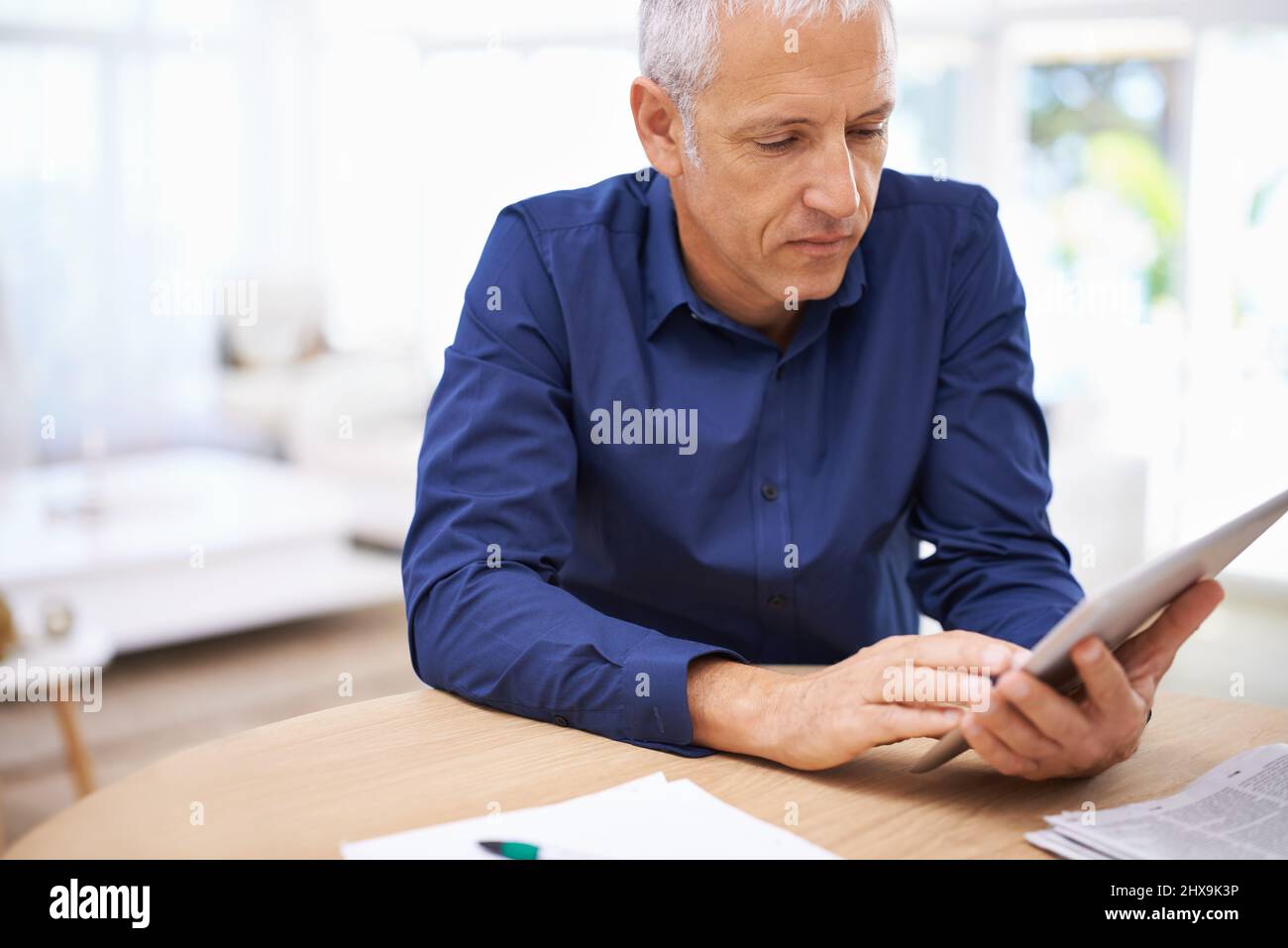 Dur au travail, même à la maison. Prise de vue d'un homme mûr à l'aide d'une tablette numérique à la maison. Banque D'Images