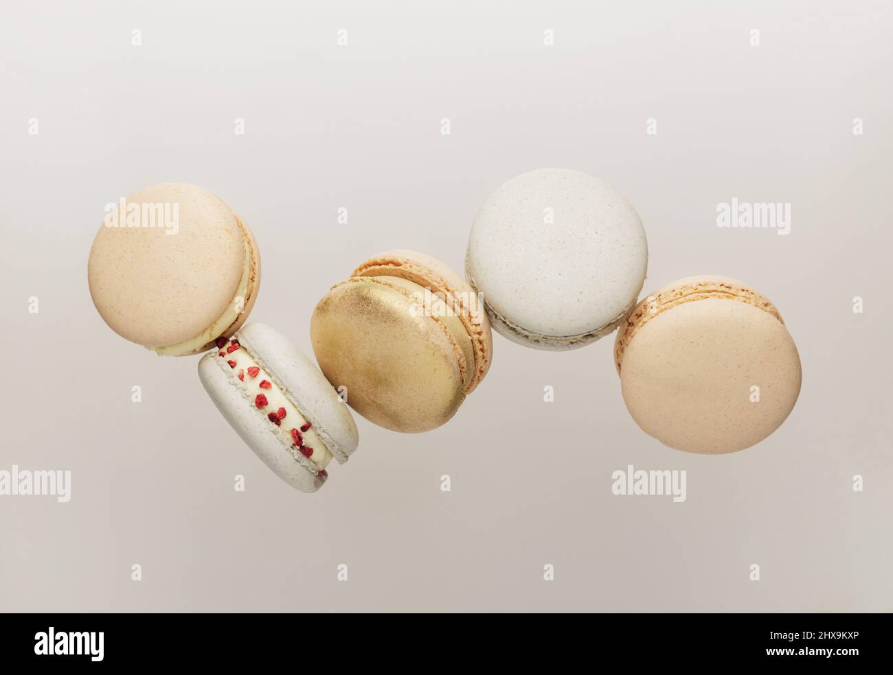 Cookies macaron blancs, jaunes, dorés volant, tombant en mouvement ou lévitant. Petits gâteaux de macaron français colorés et sucrés. Arrière-plan beige clair. Coupe brisée, pièces mordues, moitiés. Photo de haute qualité Banque D'Images