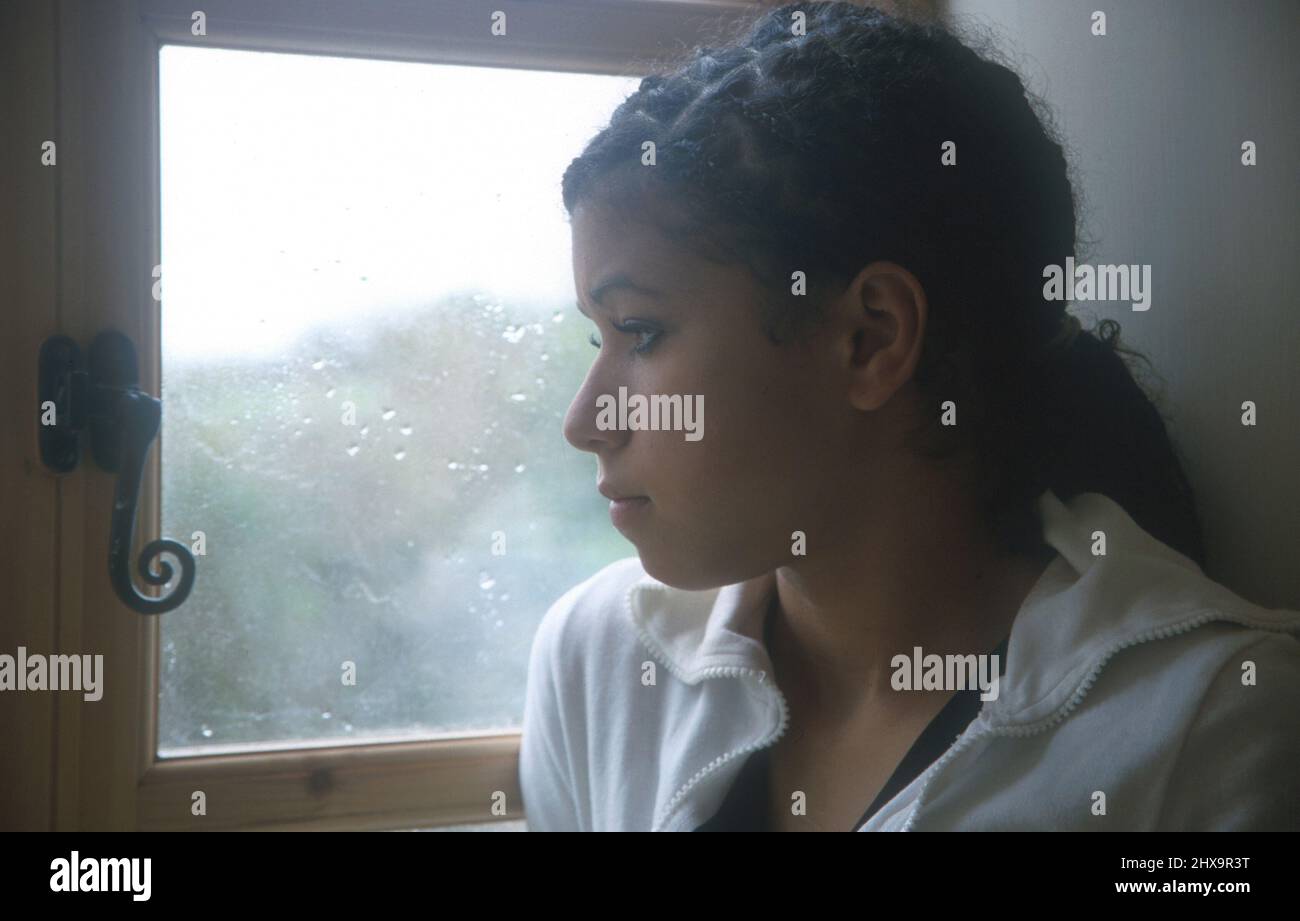 malheureuse adolescente biraciale regardant par la fenêtre le jour de pluie Banque D'Images