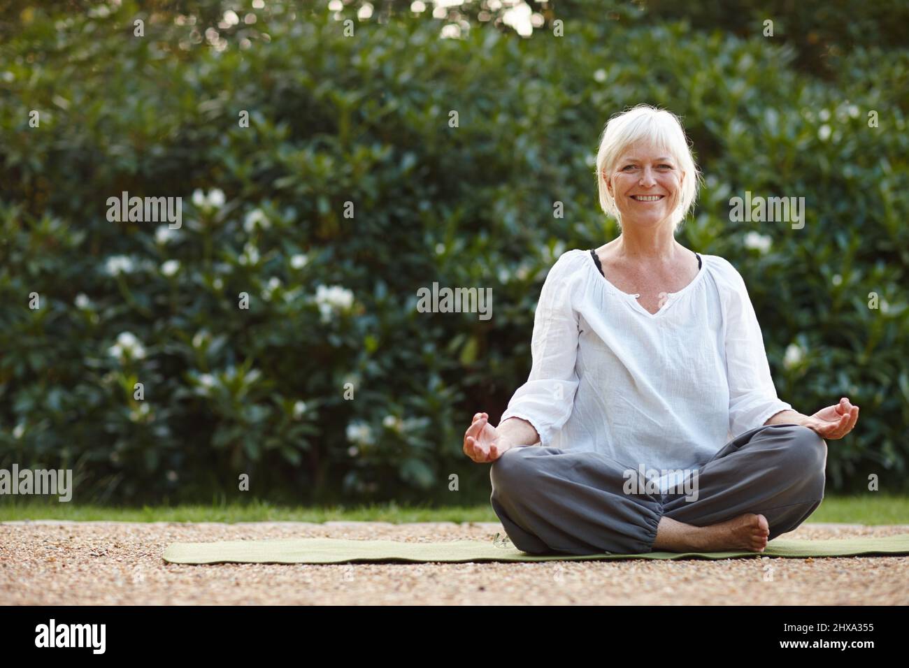 Faire ses exercices de pleine conscience en plein air. Portrait d'une femme mûre attrayante assise dans la position de lotus à l'extérieur. Banque D'Images