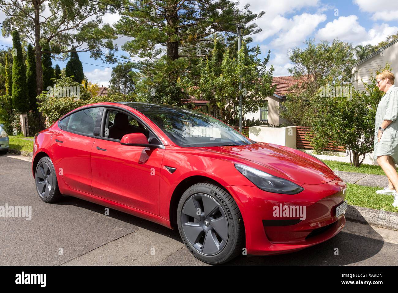 2022 voiture rouge Tesla modèle 3 dans une rue de Sydney avec une dame propriétaire conducteur approchant de la voiture, NSW, Australie Banque D'Images