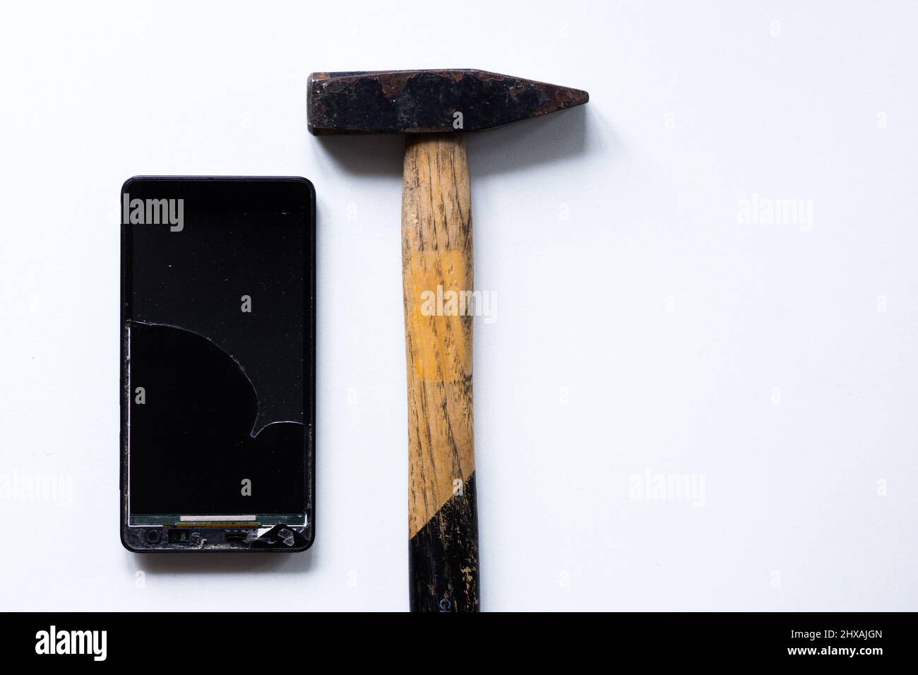 Téléphone portable cassé sur fond blanc et marteau Banque D'Images