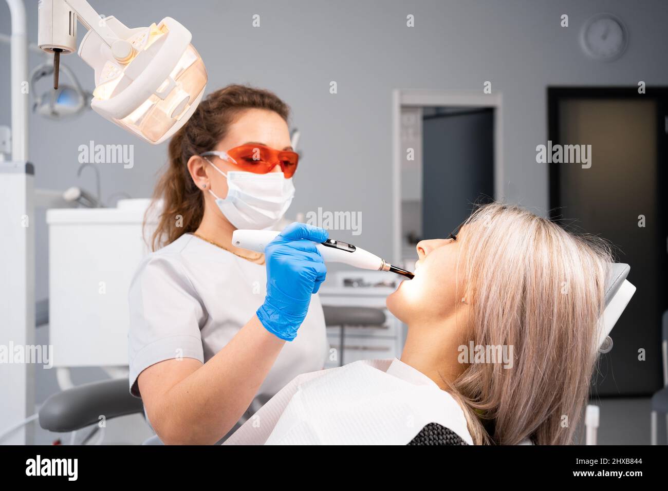 Une femme dentiste traite une cavité dentaire avec des gants bleus et un masque de protection. Traitement des caries chez le dentiste dans le bureau d'une clinique dentaire. Utilisations Banque D'Images