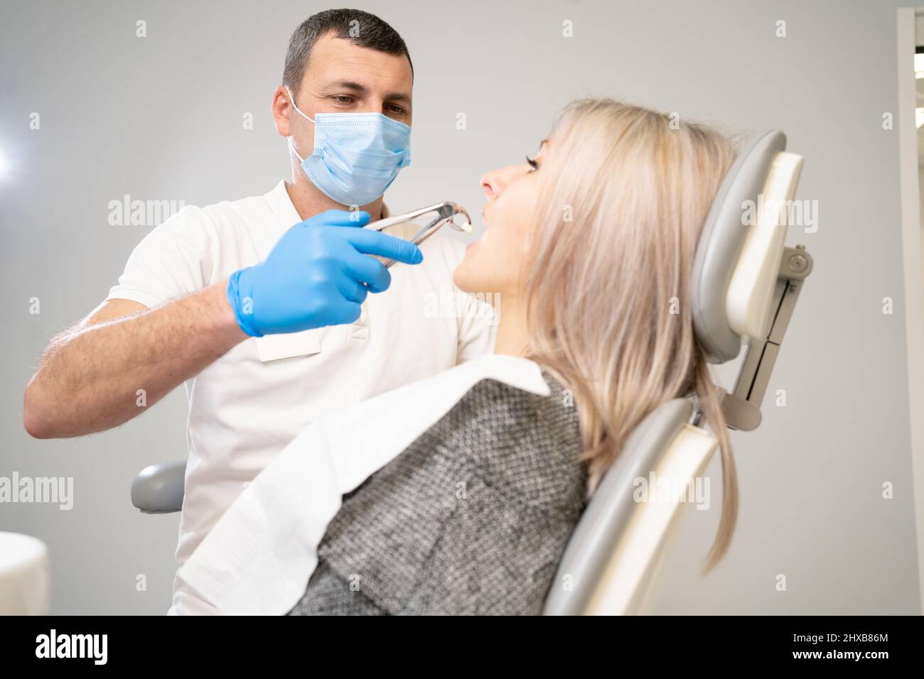 femme en clinique dentaire. Un dentiste en gants bleus en latex enlève sa dent avec un rétracteur buccal et des pinces. Banque D'Images femme en clinique dentaire. Un dentiste en gants bleus en latex enlève sa dent avec un rétracteur buccal et des pinces. Banque D'Images