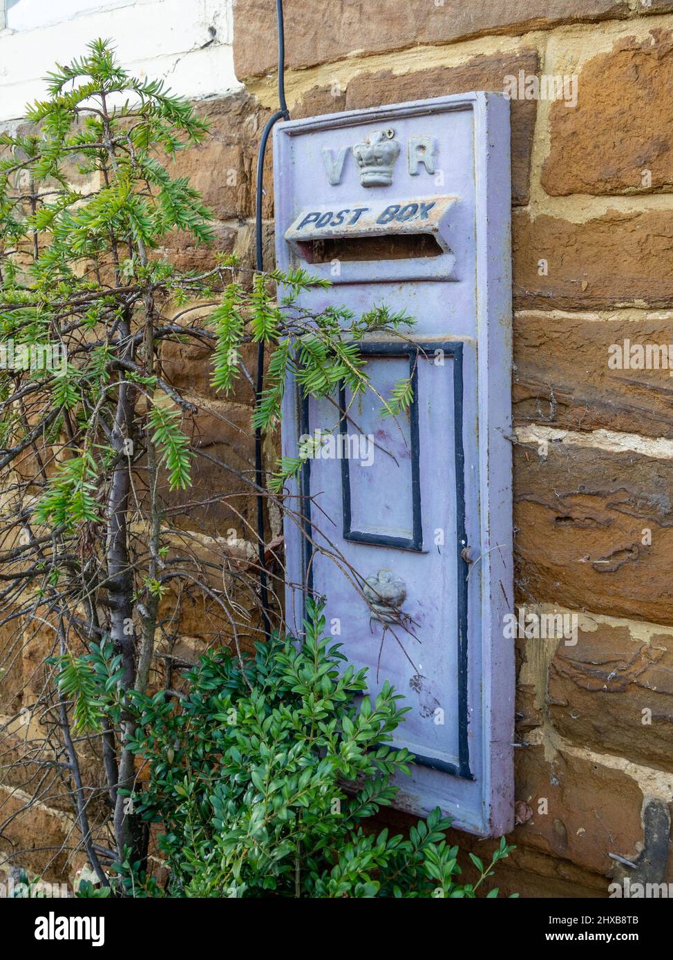 Une boîte aux lettres victorienne, peinte dans une couleur pourpre inhabituelle, est érigée dans un mur de pierre dans le village de Great Brington, dans le Northamptonshire, au Royaume-Uni Banque D'Images