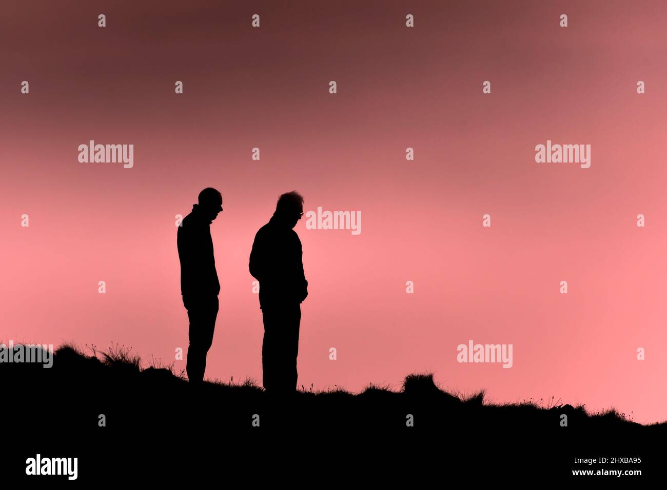 Deux personnes se tenant sur le sentier côtier ont silhoueté contre un ciel coloré à la fin de la journée à Newquay, en Cornouailles. Banque D'Images
