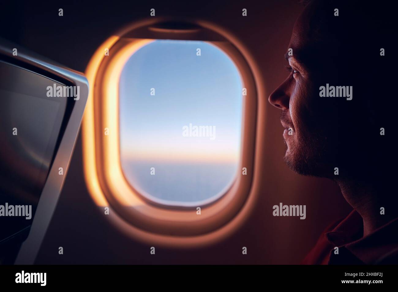 Portrait de l'homme voyageant en avion. Passager regardant à travers la fenêtre de l'avion pendant le vol au lever du soleil. Banque D'Images