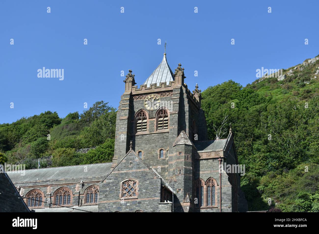 Proche de l'église St John's, Barmouth, pays de Galles. La tour de l'église se tient fière d'une journée d'été claire avec des arbres verts et un ciel bleu clair Banque D'Images