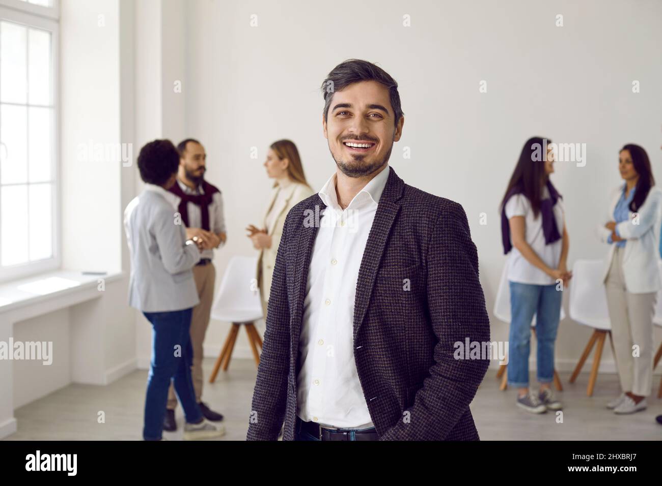 Portrait d'un homme d'affaires heureux en costume debout au bureau, souriant et regardant l'appareil photo Banque D'Images