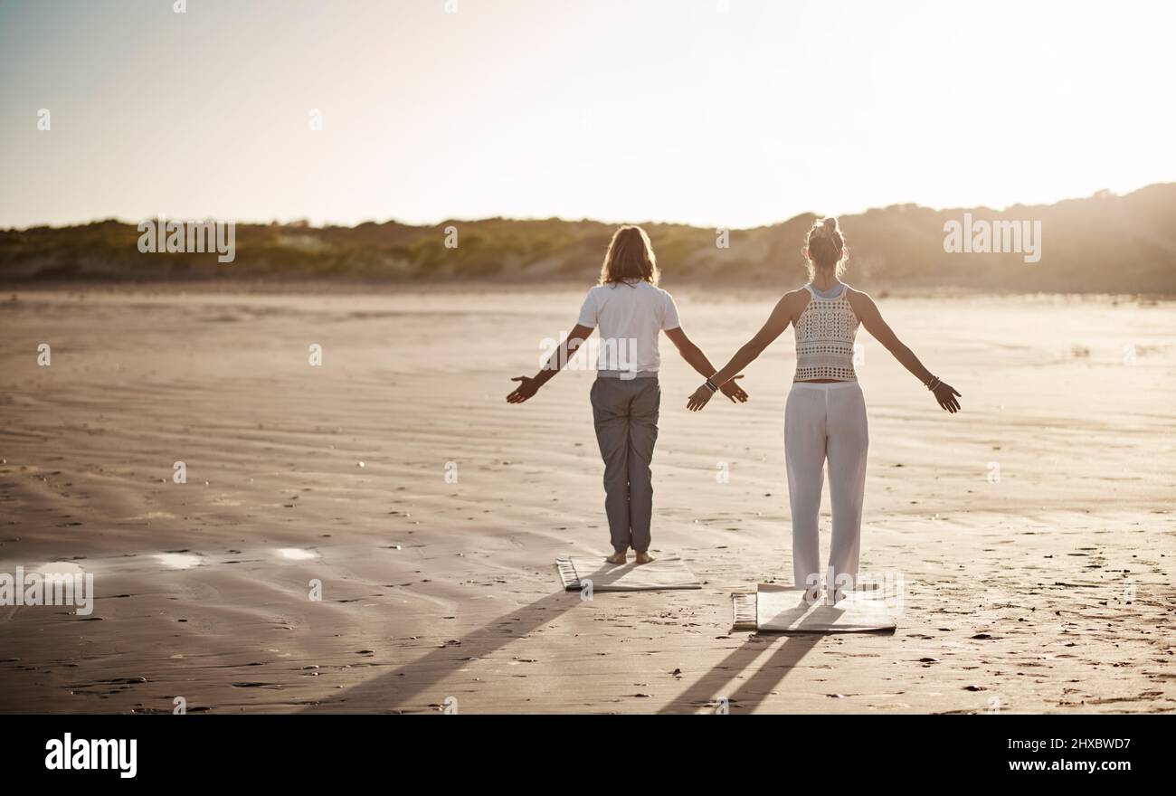 Suivez votre chemin paisible avec le yoga. Photo d'un couple méconnaissable pratiquant le yoga sur la plage. Banque D'Images