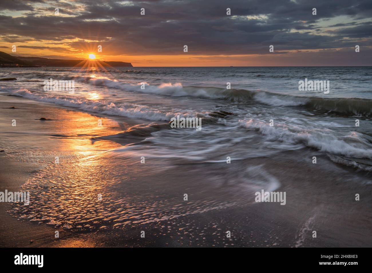 Coucher de soleil Golden hour sur la plage de Whitby. Ciel chaud et vagues douces et douces le long d'une côte sablonneuse avec de grandes rochers. Banque D'Images