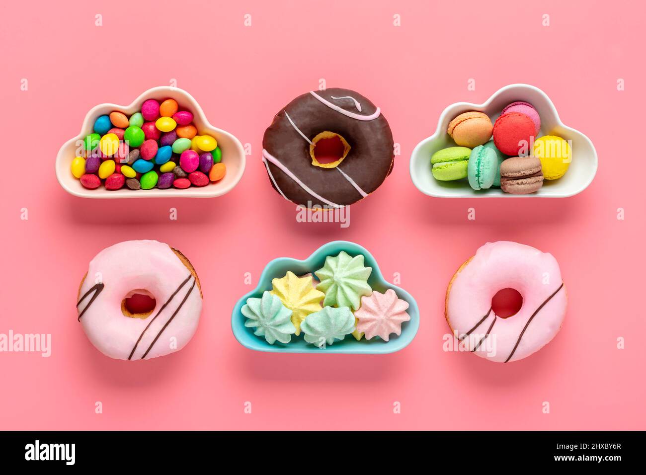 Bonbons et meringues dans un bol en forme de nuage, chocolat avec garniture colorée et donut rose isolé sur fond rose plat Lay Top View Knolling Banque D'Images