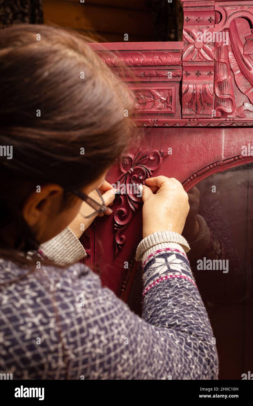 Vieille femme mains accrochent des ornements sculptés à bois rouge clair carton couleur avec le verre rond en face dans la maison de chalet en bois. Réutilisation des objets anciens Banque D'Images