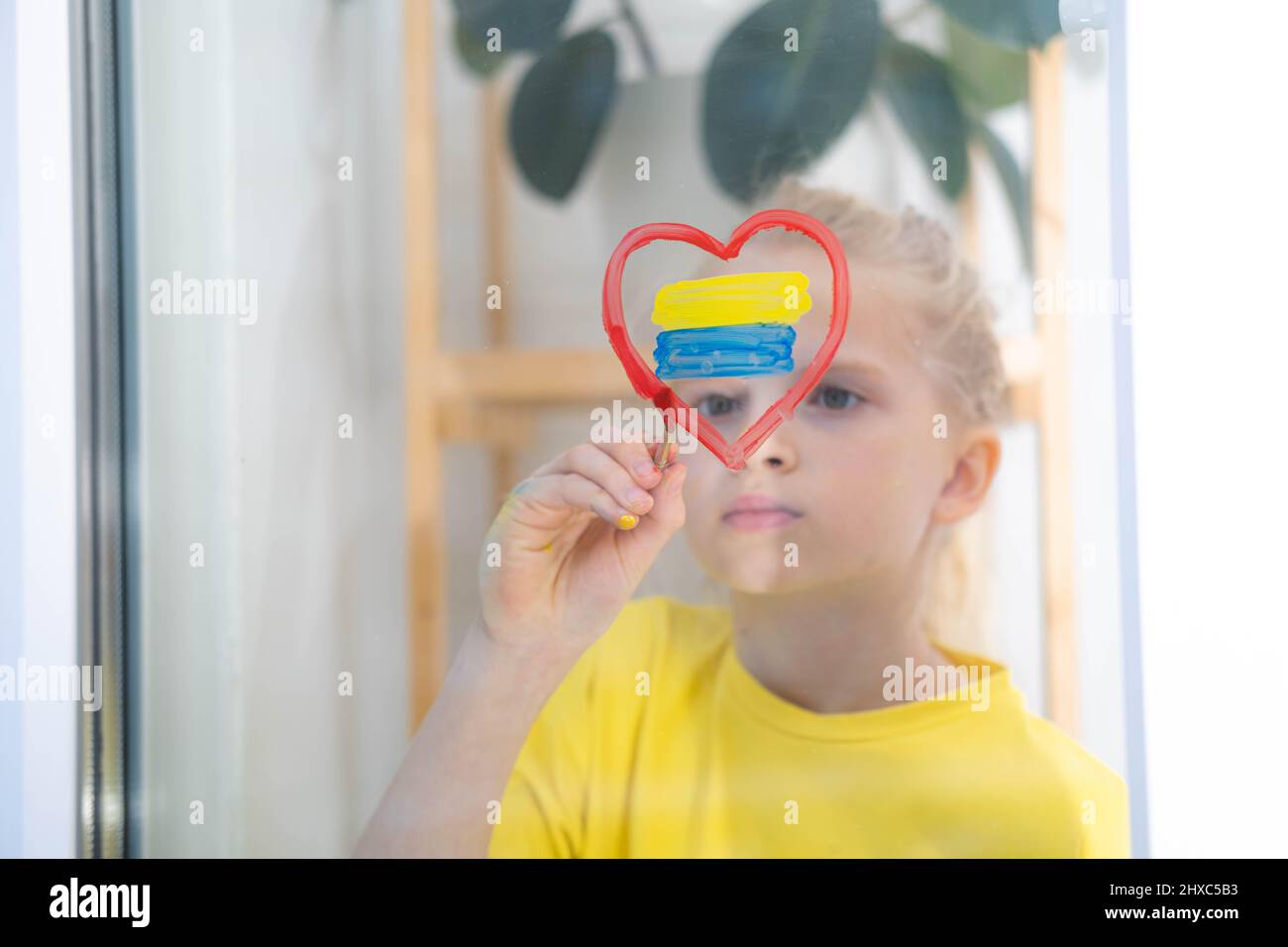 Une jeune fille patrant le drapeau de l'Ukraine sur la fenêtre a bouleversé et survit à la guerre Ukraine Russie. Banque D'Images