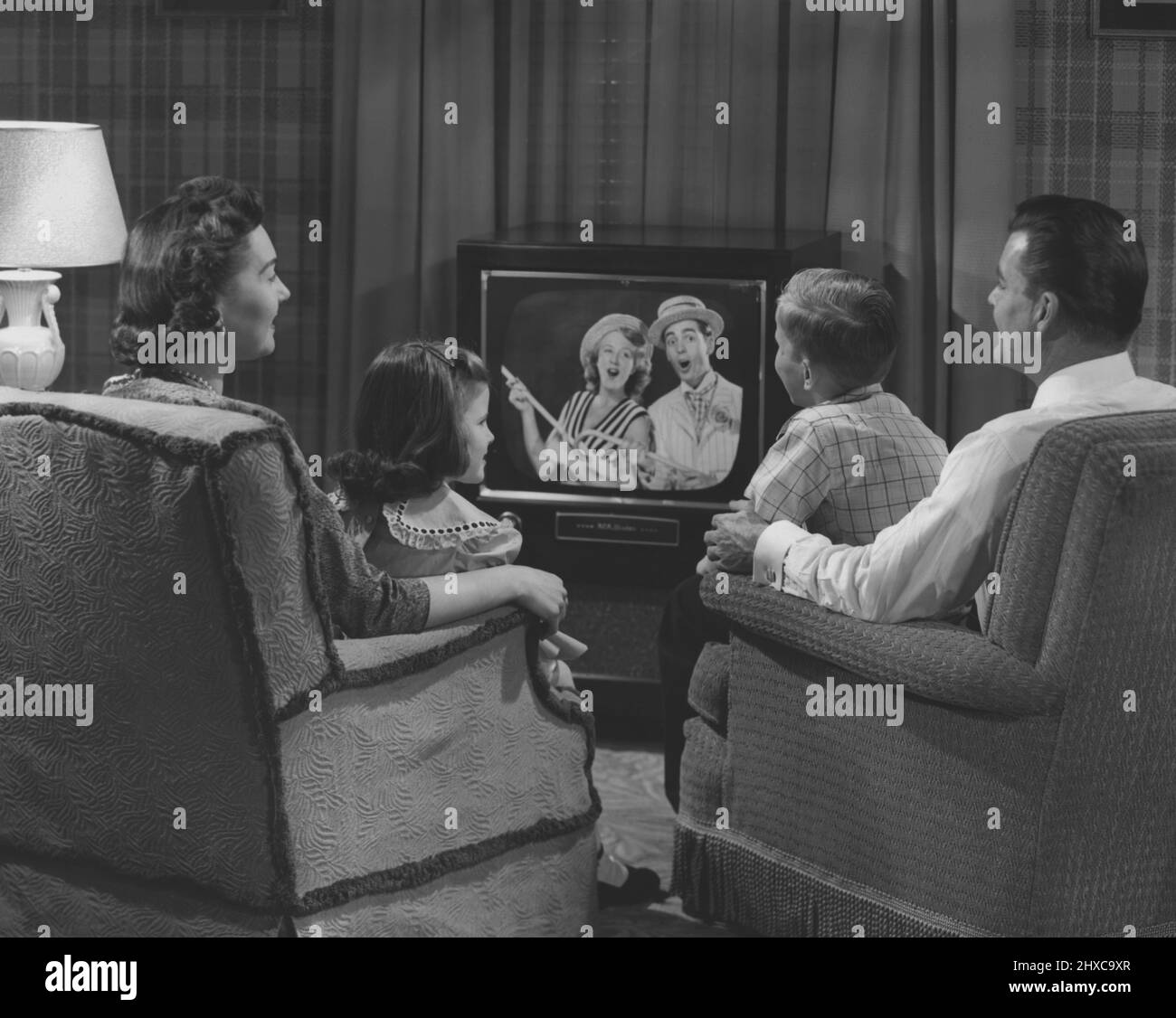Maman, papa, garçon et fille bien habillée assis dans le salon regardant une émission de télévision Banque D'Images