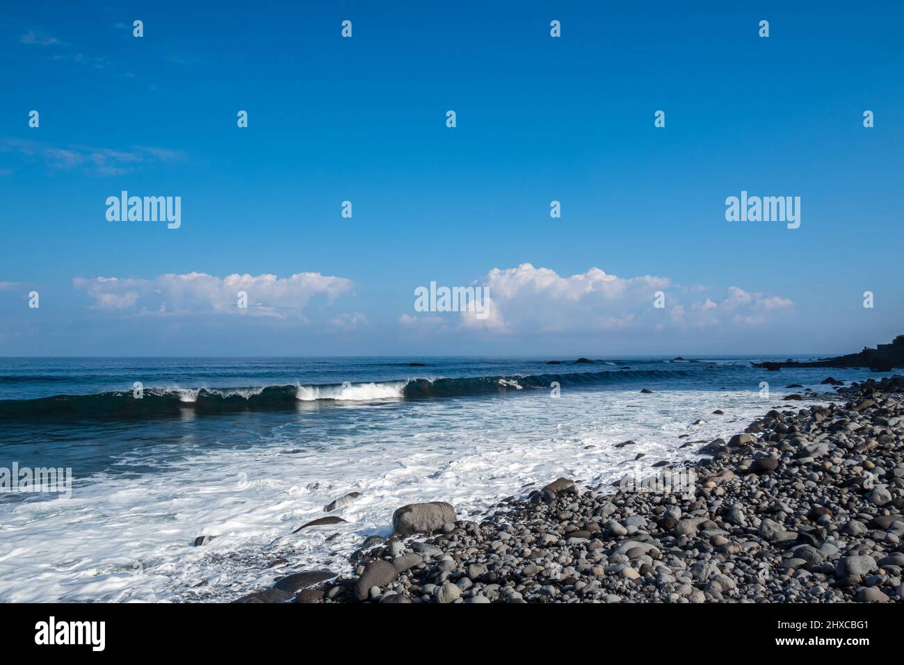 Côte avec des pierres polies d'eau de mer, en arrière-plan une vague entrante, un horizon et un ciel bleu avec quelques nuages, image de Sao Vincente Madeira po Banque D'Images