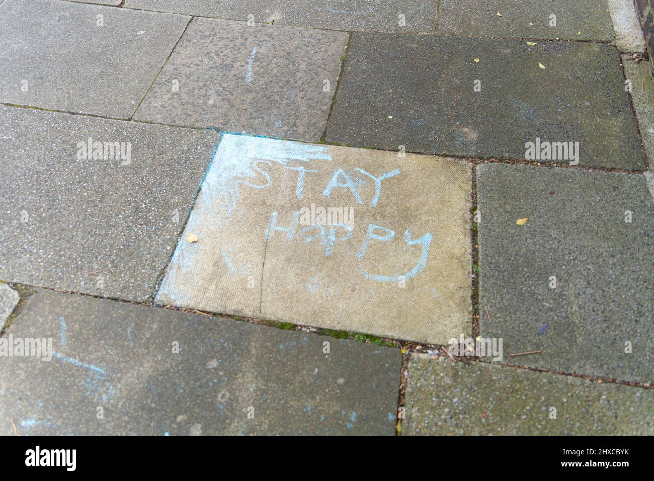 Une pierre pavée dans un pavé sur une rue de banlieue avec craie écrivant: 'Stay Happy'. Concept de bonne santé mentale. Banque D'Images