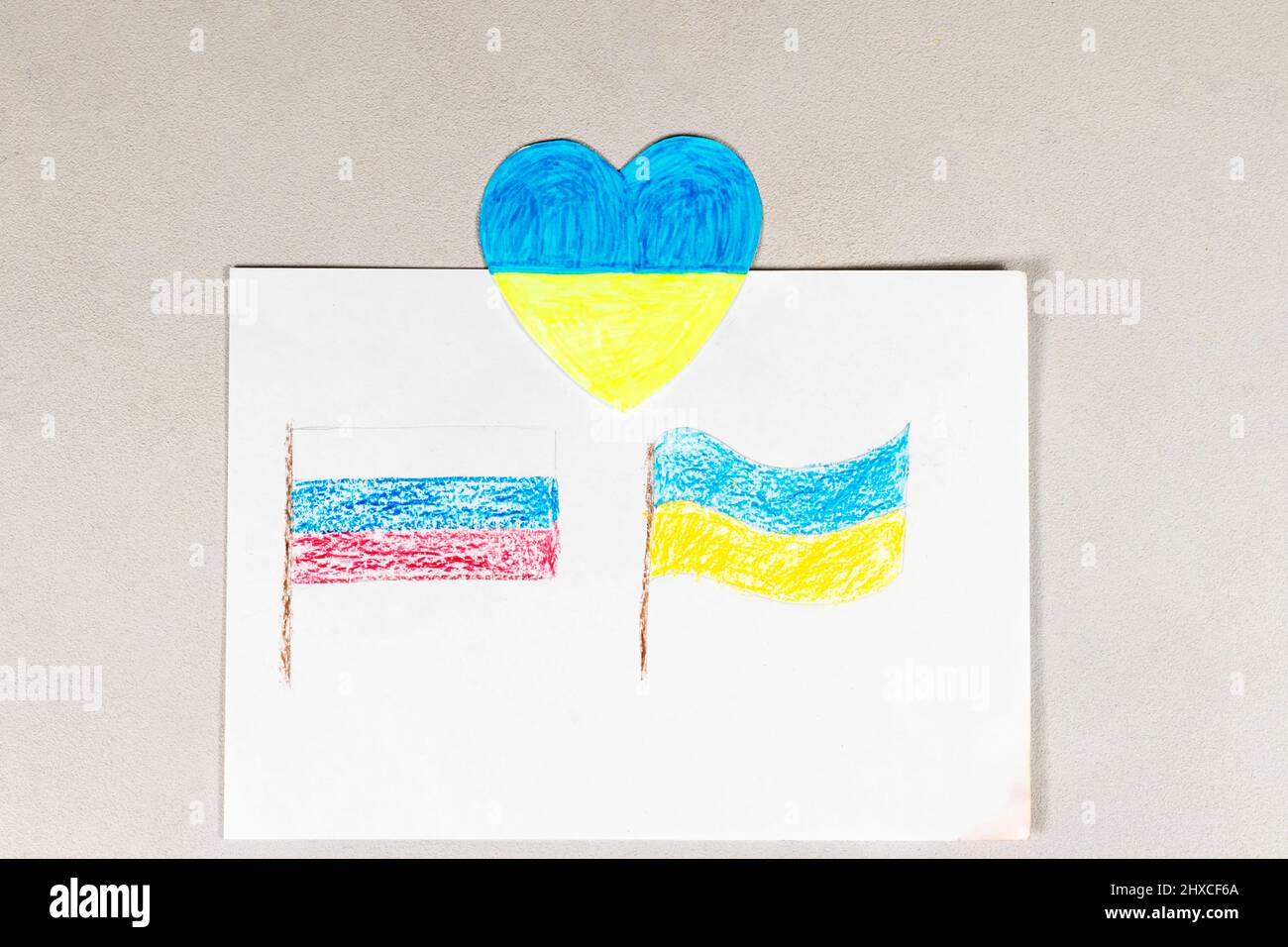 Un enfant fait un signe de coeur avec ses mains sur un dessin de deux drapeaux de l'Ukraine et de la Russie gros plan. Vue de dessus. Les enfants contre la guerre. Banque D'Images