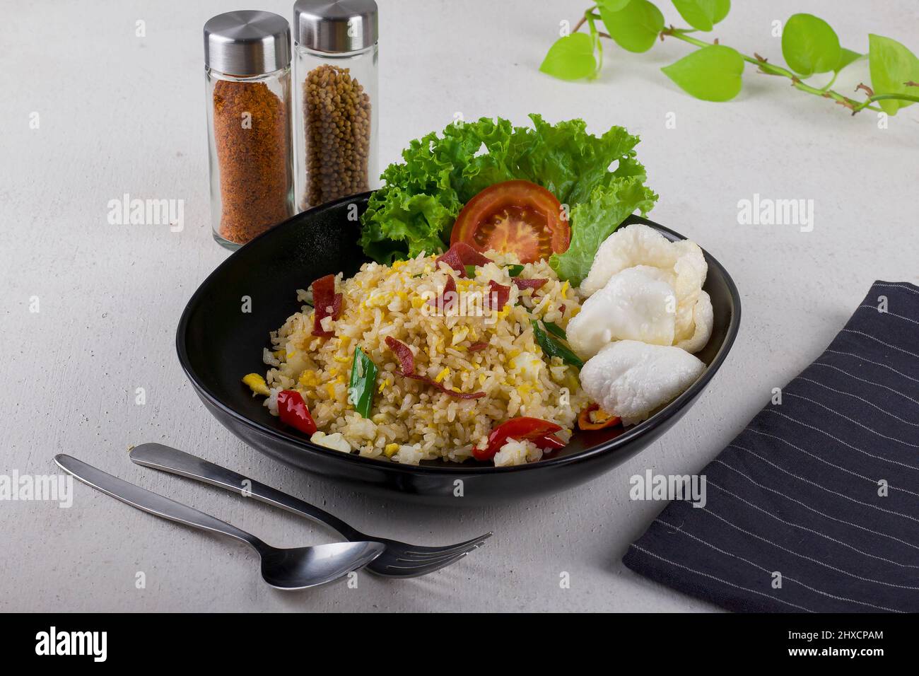 sauté de riz frit asiatique épicé avec du bœuf fumé, tranche de tomate rouge fraîche, laitue verte fraîche et craquelins blancs dans une assiette ovale noire Banque D'Images