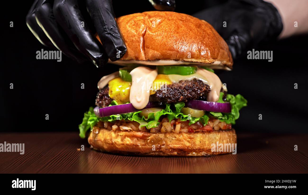 Burger d'artisanat est cuisson sur fond noir. Composé : sauce rouge salsa, laitue, oignon rouge, cornichon, fromage, piment poivron vert, air bun et marbré de moi Banque D'Images