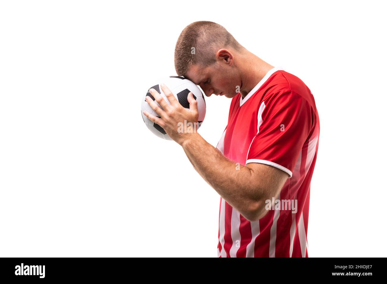 Vue latérale d'un jeune athlète caucasien touchant le ballon de football sur le front sur fond blanc Banque D'Images