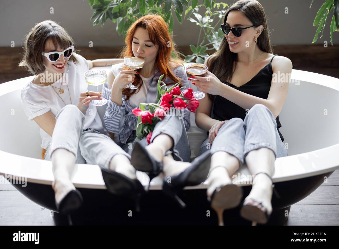 Trois jeunes amies adultes assises avec des boissons alcoolisées dans la baignoire, faisant une fête de poules ou célébrant les vacances des femmes à la maison Banque D'Images
