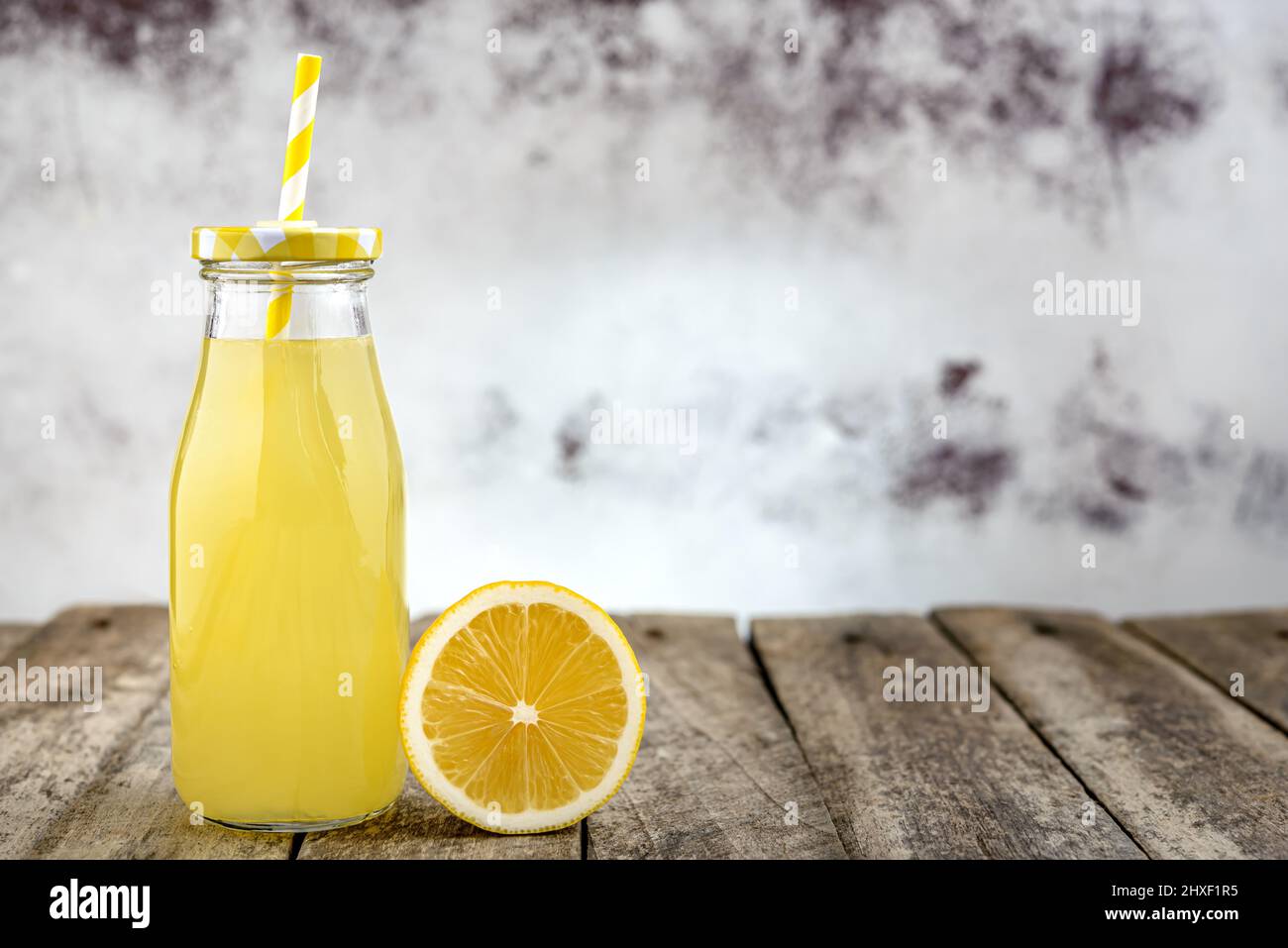 Bouteille de limonade froide avec paille et tranche de citron sur table rustique en bois. Banque D'Images