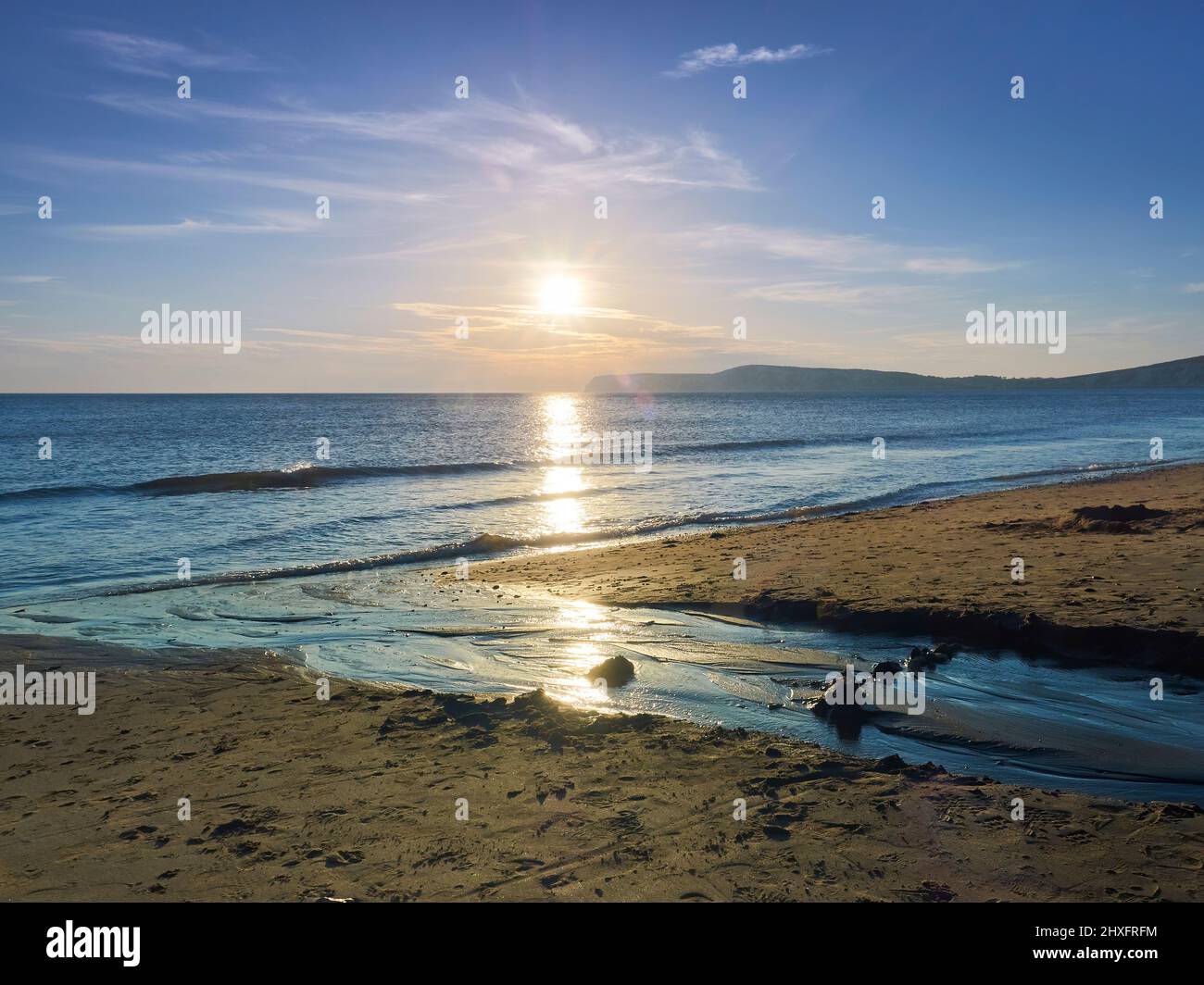 Un soleil descendant, qui se dirige vers une tournière silhouettée, jette un sentier doré scintillant à travers les eaux de Solent jusqu'à la plage de sable de Compton Bay. Banque D'Images