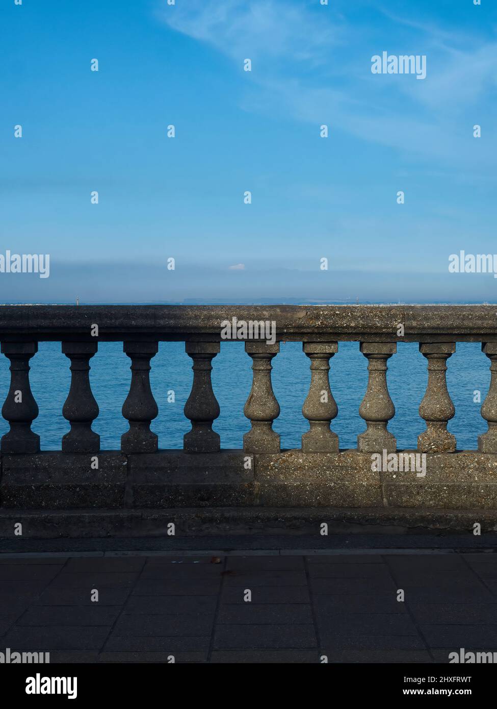 Un ciel côtier au-dessus d'une balustrade ornementale sur une esplanade du mur de mer dans un spot incliné de soleil qui met en lumière les ombres. Banque D'Images