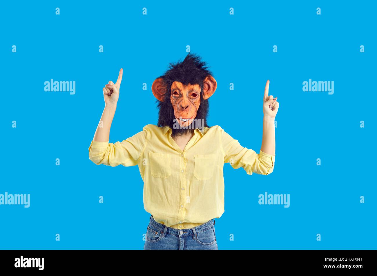 Femme portant un masque de singe drôle pointant ses index vers le haut isolés sur fond bleu Banque D'Images