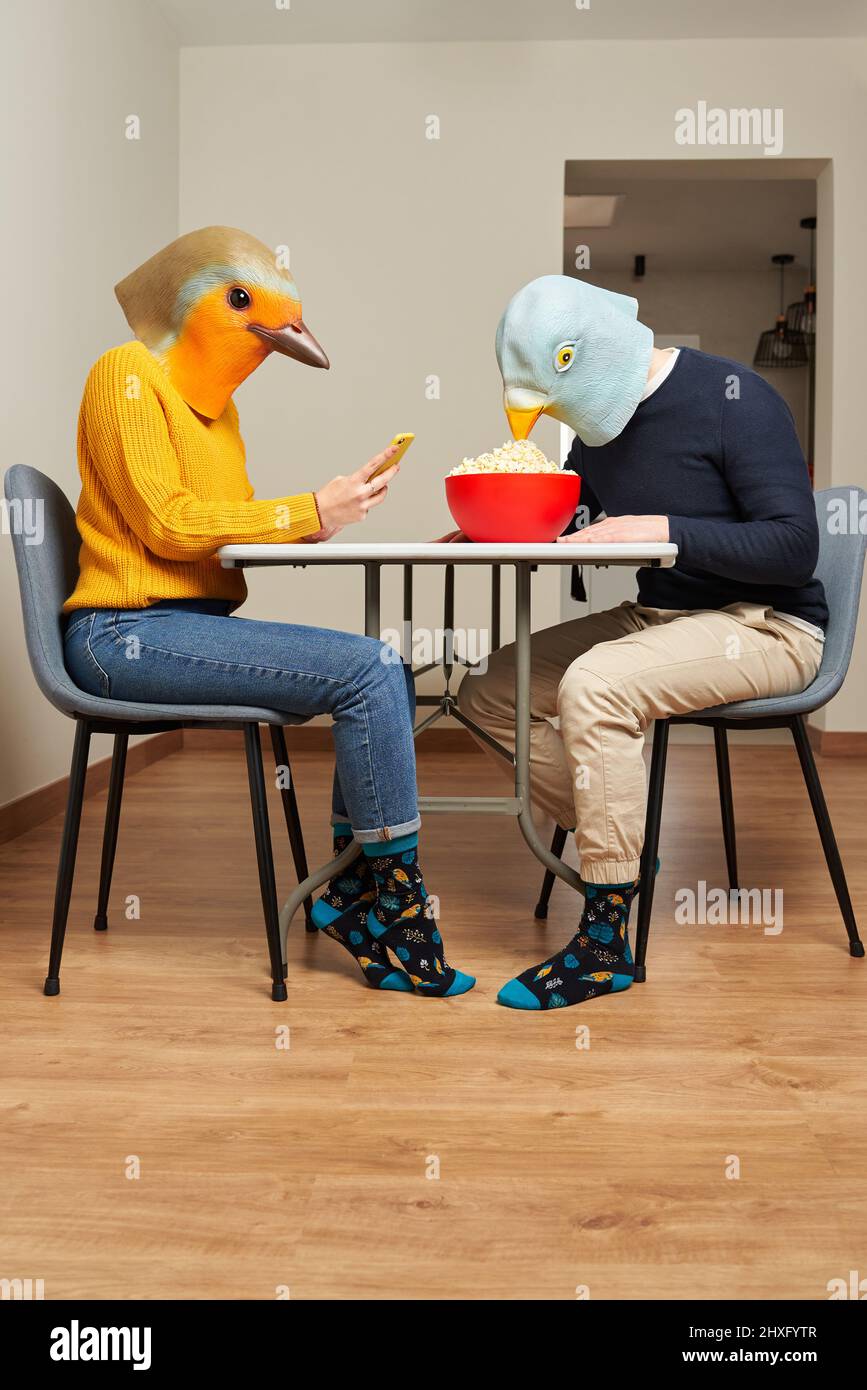 Un couple vêtu de masques pour oiseaux mange du pop-corn à la table Banque D'Images
